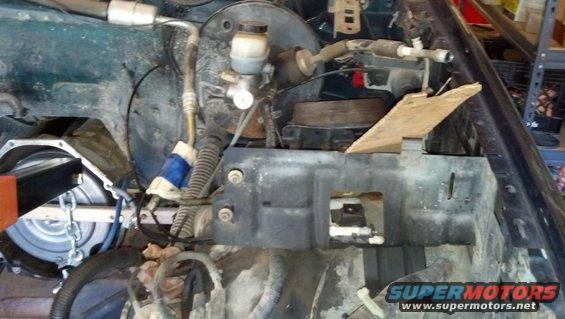 engine bay with brake master cylinder, hoses, and some engine components visible. A piece of wood is propped up