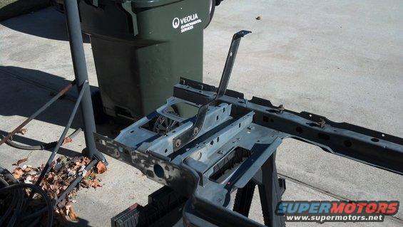 Vehicle frame section on a stand, with a trash can in the background