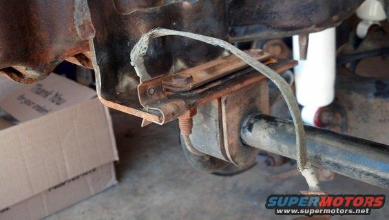 Rusty rear axle assembly with a white shock absorber and a grounding strap