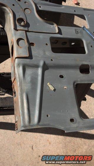 Close-up of a gray metal vehicle frame section with some rust spots. A wrench is visible on the right