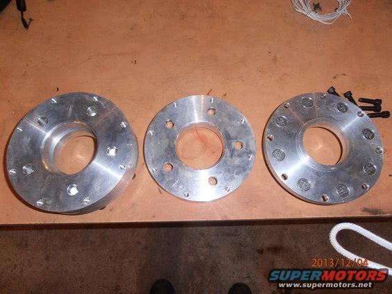 three metal wheel spacers with bolt holes on a wooden surface