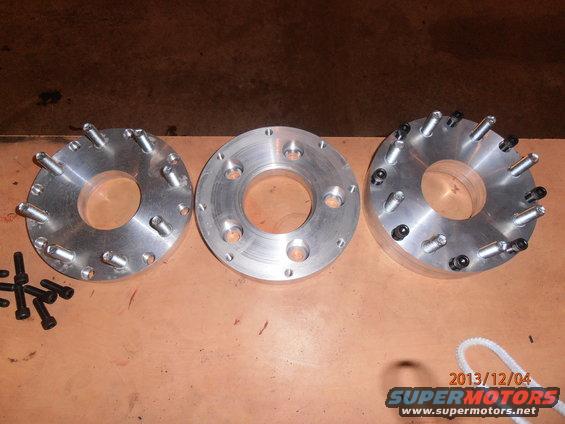 Three metal wheel spacers with bolts on a wooden surface