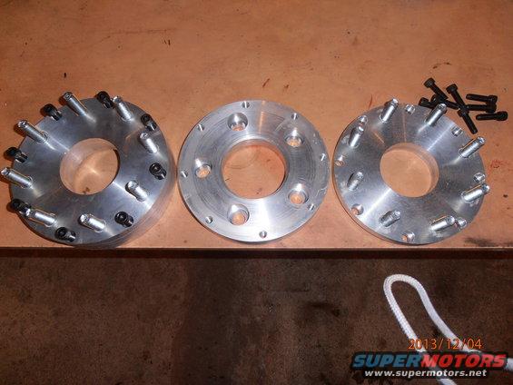 Three metal wheel spacers with bolts on a wooden surface