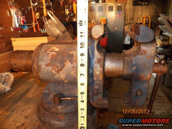 Rusty bench vise next to a measuring tape showing 12 inches