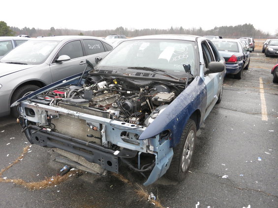 Blue Ford Crown Victoria with hood open, missing front bumper and grille. Other cars in background