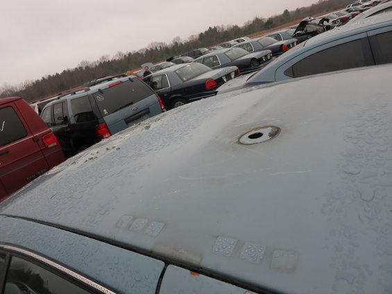 Junkyard scene with a light blue sedan in the foreground, other cars and SUVs in the background