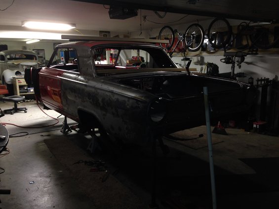 1964 Ford Fairlane body on jack stands in a garage, undergoing restoration. Another car is visible in the background