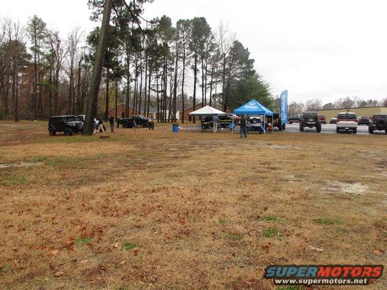 Several off-road vehicles parked in a grassy field with tents set up