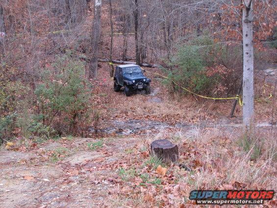 Dark blue Jeep Wrangler on a muddy trail in a wooded area
