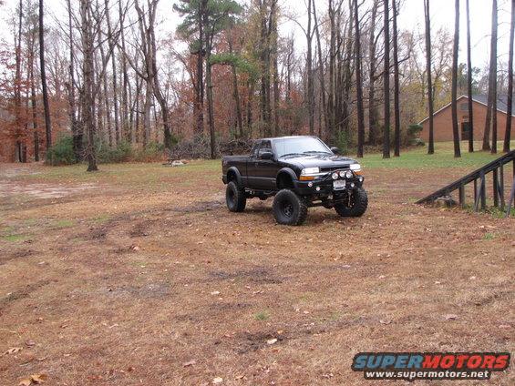 Lifted black pickup truck with large tires parked in a grassy, wooded area