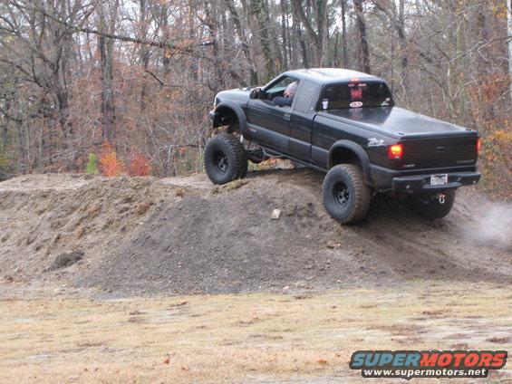 Black pickup truck with large tires climbing a dirt mound