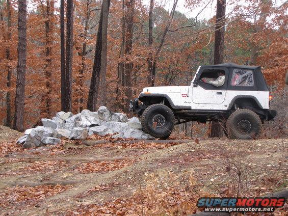 White Jeep Wrangler navigating rocks on a wooded trail