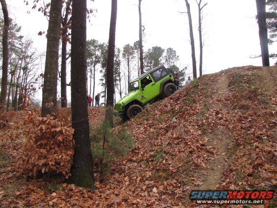 Green Jeep Wrangler driving up a leaf-covered hill in a wooded area