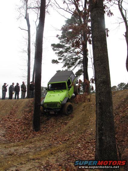 Green Jeep Wrangler climbing a dirt hill, with a group of people watching