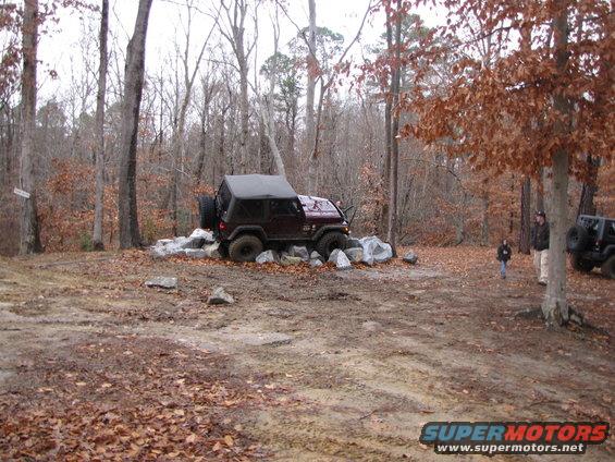Dark red Jeep Wrangler on rocks with soft top, spare tire on rear