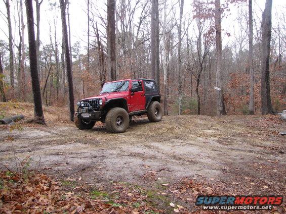 Red Jeep Wrangler with off-road tires on a dirt path in a wooded area