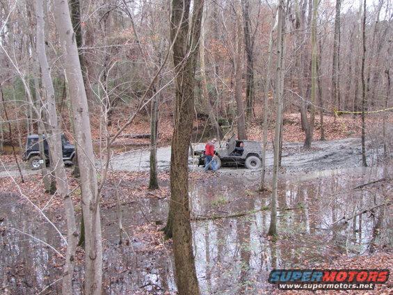 Two Jeeps navigating a muddy forest trail with standing water