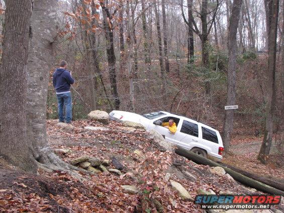 White SUV stuck on a wooded trail with a person watching