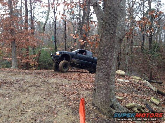 Black pickup truck with lifted suspension driving off-road on a dirt path with trees and fallen leaves