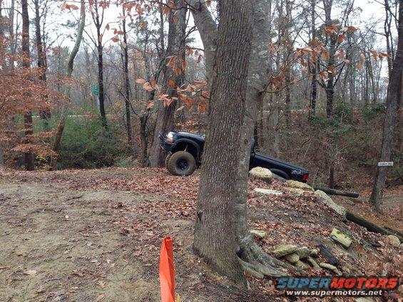 Black pickup truck tilted on a wooded trail, front wheel turned