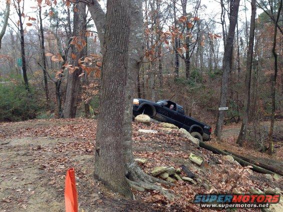 Black pickup truck navigating an off-road obstacle course with large rocks and fallen logs