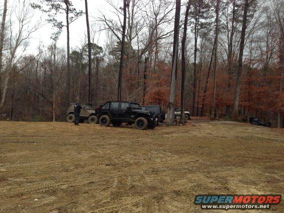 Several off-road vehicles parked in a muddy clearing surrounded by trees