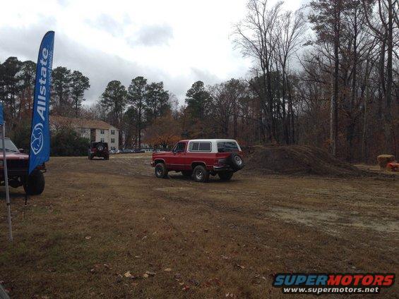 Red and white SUV parked on dirt lot, spare tire mounted on rear door. Another SUV is visible in the background