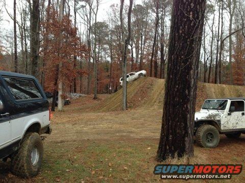 Black and white SUV parked in a wooded area with a white Jeep and another vehicle on a dirt ramp