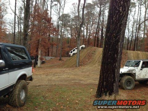 Two off-road vehicles, one black and white SUV in foreground, white Jeep on dirt ramp in background