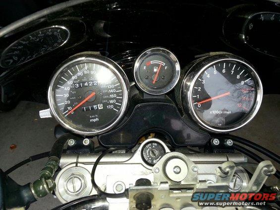 Motorcycle dashboard with speedometer showing 31422 miles and 115 mph, tachometer, and fuel gauge