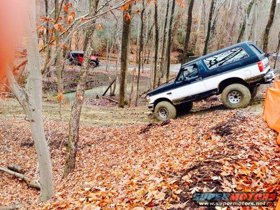 Black and white Ford Bronco climbing a dirt hill, another red Jeep in background