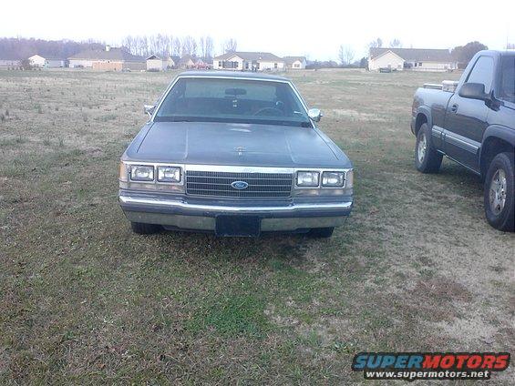 1980s Ford sedan parked on grass next to a pickup truck