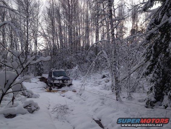 Dark SUV with winch cable stuck in snowy forest path