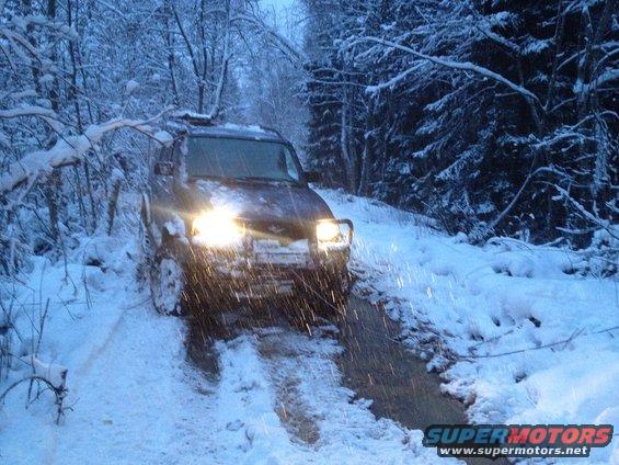 SUV driving on a snowy path in the woods, headlights on