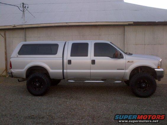 Silver crew cab pickup truck with camper shell, lifted suspension