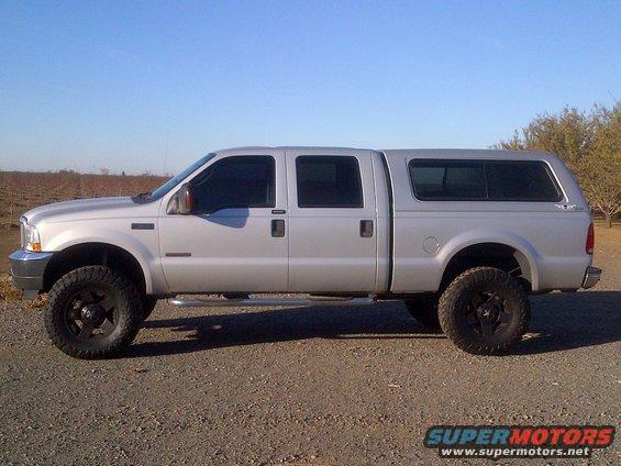 Silver crew cab pickup truck with a camper shell, lifted with large tires