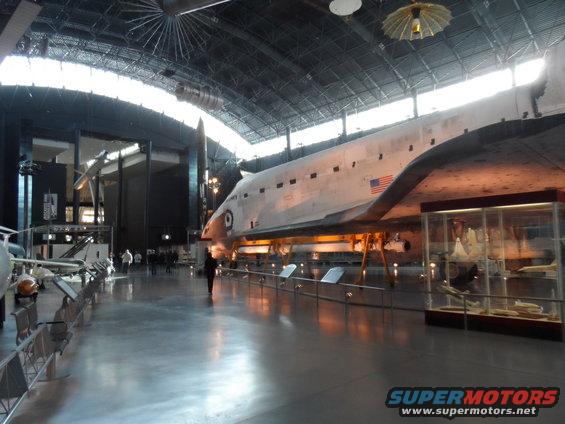 Space shuttle in a museum, viewed from the side, with an American flag on its fuselage