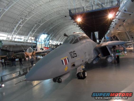 F-14 Tomcat fighter jet with number 105 on fuselage, parked indoors with other aircraft in background