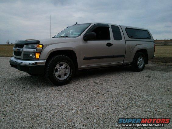 Silver Chevrolet Colorado pickup truck, extended cab, with a black camper shell. Front fender has a bug deflector