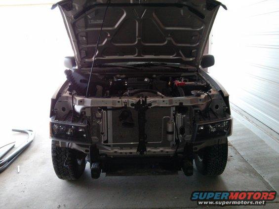 Truck front end disassembled, hood open, showing engine and radiator. Headlights removed