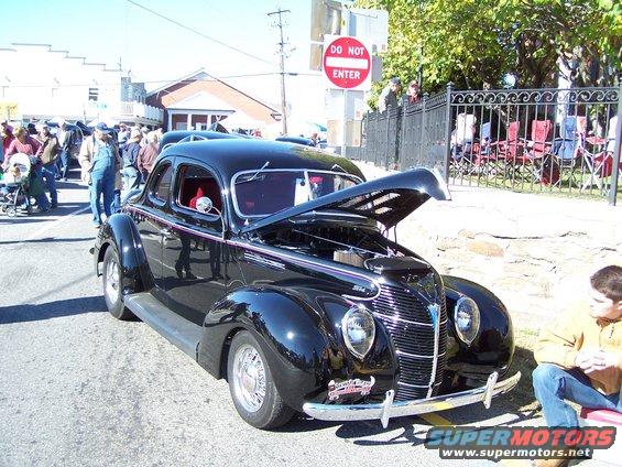 Black 1940 Ford Coupe with hood open, parked on street with people around