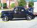 1971 Ford Ranchero - A black 1939 Ford Coupe with its trunk open is parked on a street next to a building.