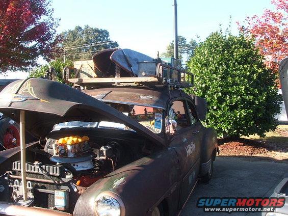 Rusty car with open hood, roof rack, and surfboards