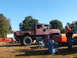 1971 Ford Ranchero - A large maroon military truck is parked on a grassy field with people gathered around, alongside other vehicles under a clear blue sky.