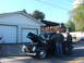 1971 Ford Ranchero - Two men examine the engine of a black pickup truck parked in front of a garage.