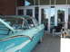 1971 Ford Ranchero - A vintage two-tone turquoise and white coupe with its hood open is parked in front of a building with glass doors.