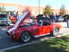 1971 Ford Ranchero - Red convertible sports car with white stripes at a car show, hood open, with other vehicles around.