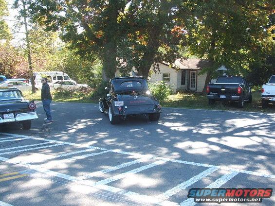 Black hot rod coupe parked on street, another classic car to the left, pickup trucks in background