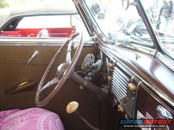 car interior with large steering wheel, dashboard with vents, and a pink blanket on the seat