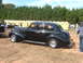 1971 Ford Ranchero - A classic black sedan from the 1940s is parked outdoors with other vehicles and portable restrooms in the background.